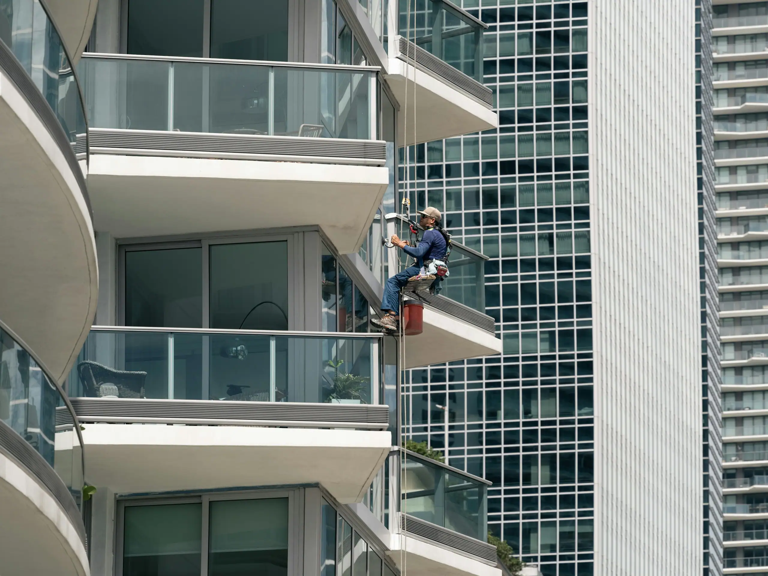 A rope-access technician working on the glass balustrades of a residential tower